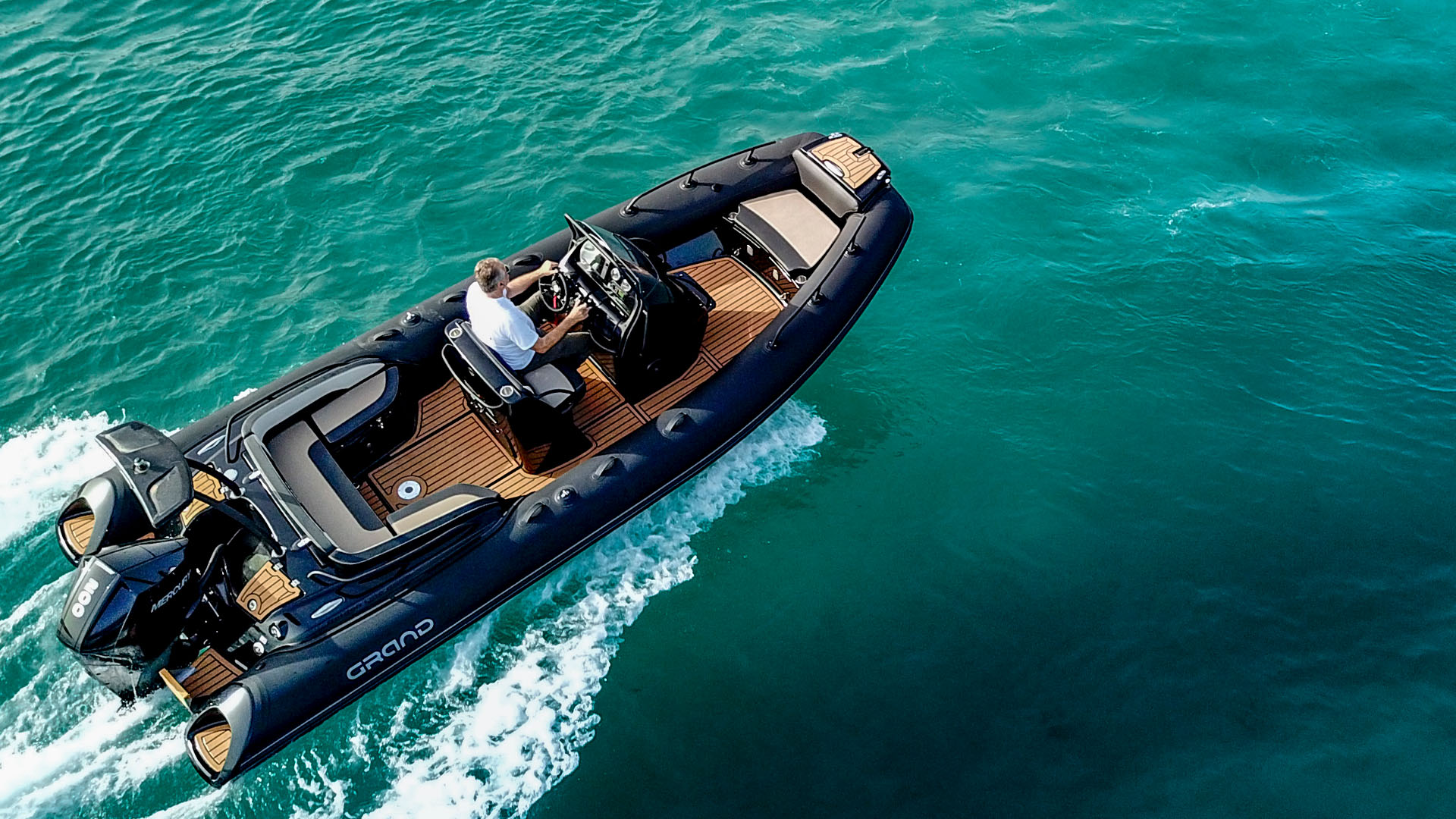 A Grand G650 RIB in black with tan sea deck flooring cruising on turquoise water