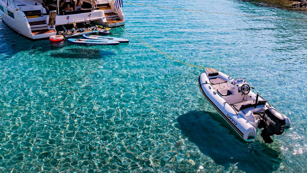 A Grand G380 - a yacht tender in the Grand RIBs range - with white tubes on light blue water, serving as a tender behind a catamaran yacht