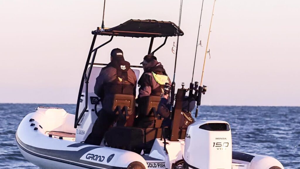 A Grand D600 inflatable fishing boat in white with two passengers on board and rods at the stern and on the t-top