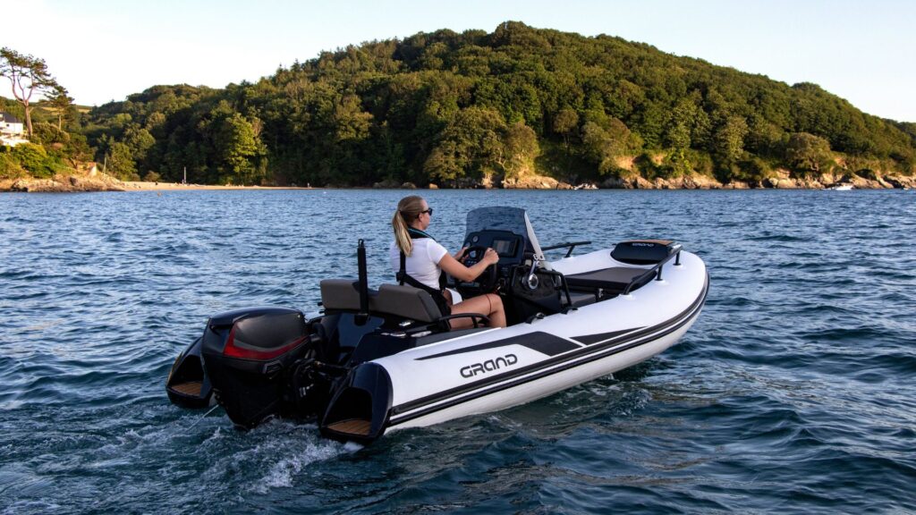 A small white rigid inflatable boat on the water with a female passenger driving