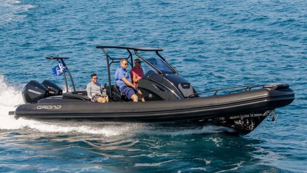 A top selling luxury cruiser boat by Grand - the Grand G850 - on the water with black tubes. Three passengers on board