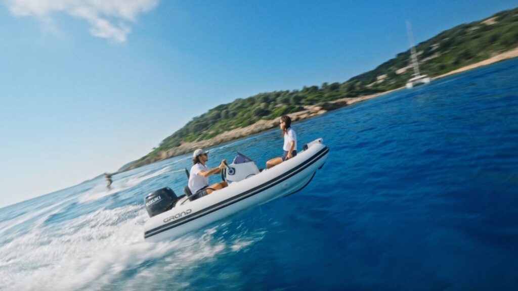 A Grand G340 inflatable watercraft serving as a sports RIB with two passengers on board and a waterskiing passenger in the water behind them