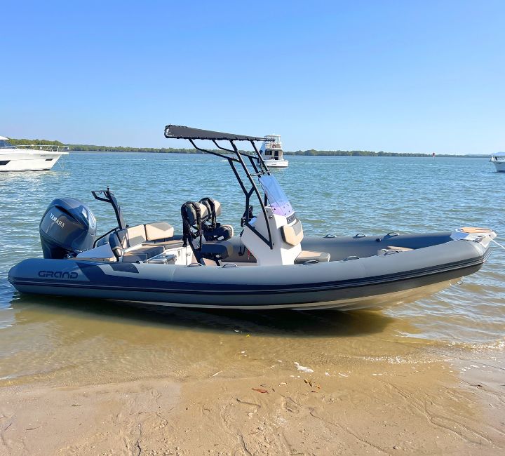 The Grand D600 for sale with dark grey tubes and a t-top with Yamaha 150HP outboard sitting on the beach