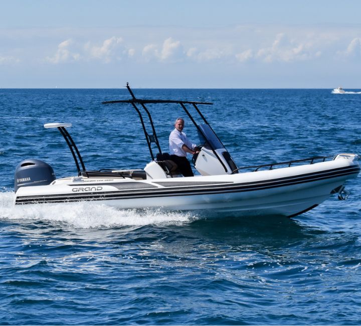 Grand G680 with white tubes on the water, with a passenger onboard sitting under a t-top