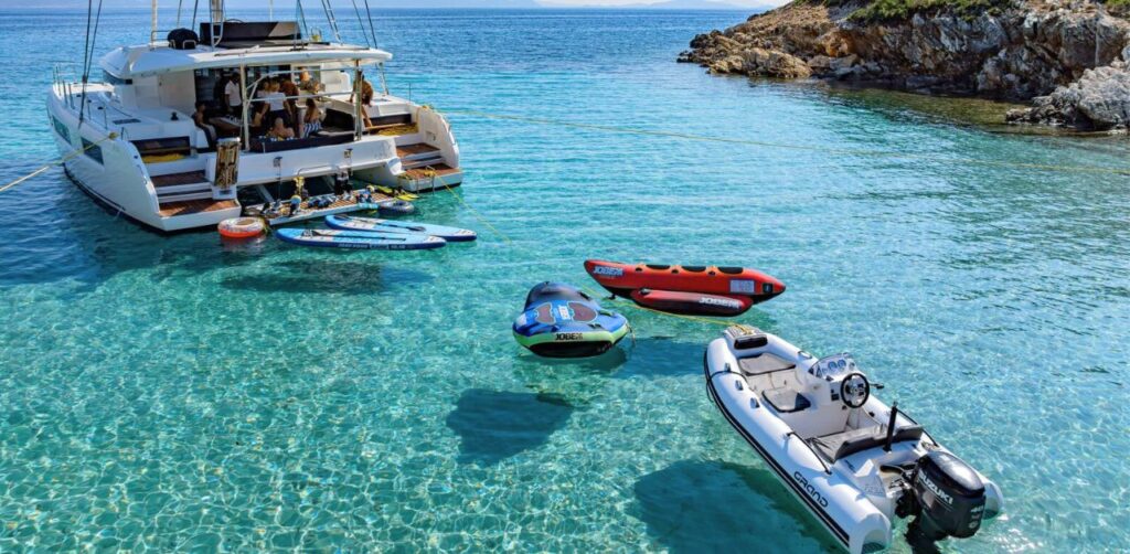 A white Grand inflatable boat serving as a bot tender behind a catamaran yacht