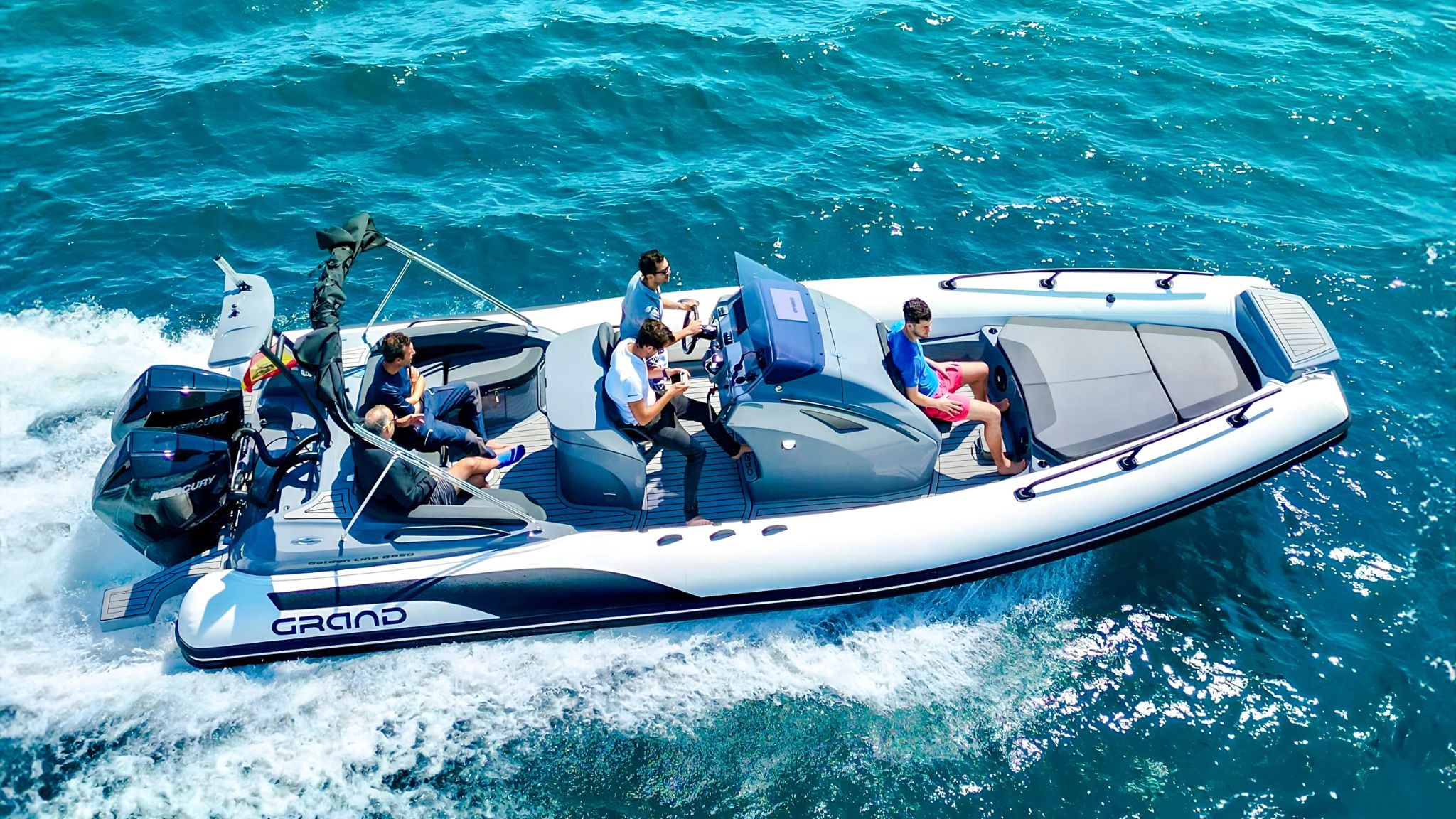 A white and grey Grand G850 rigid inflatable boat travelling through the water with five passengers on board