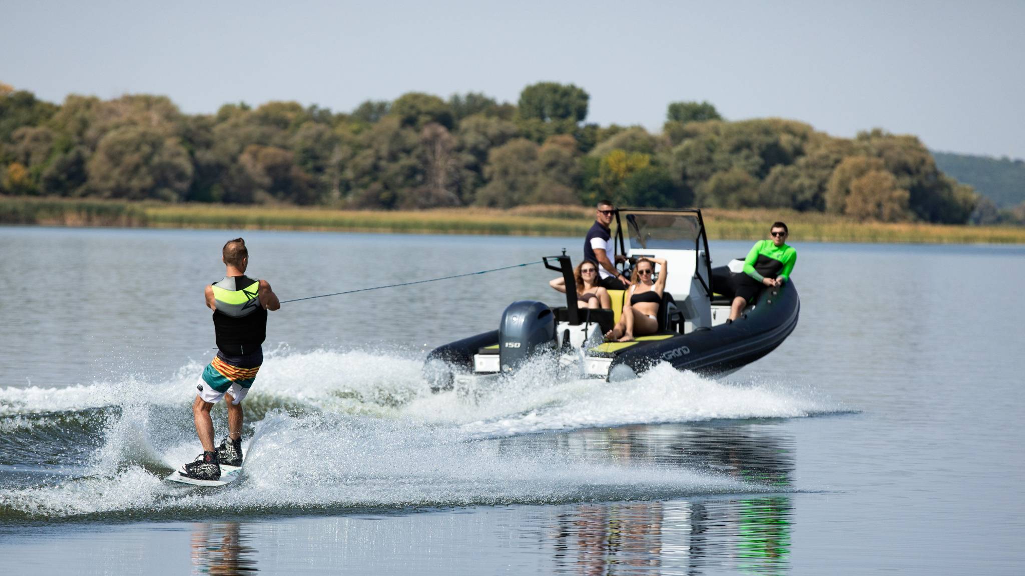 A wakeboarder behind a Grand D600 boat with passengers onboard watching