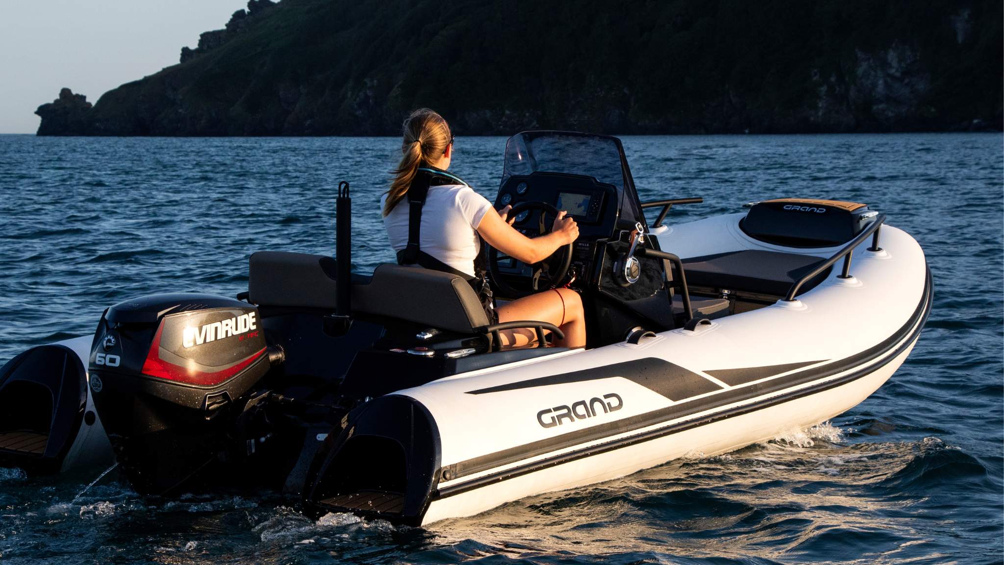 A woman driving the Grand G420 boat at sunset