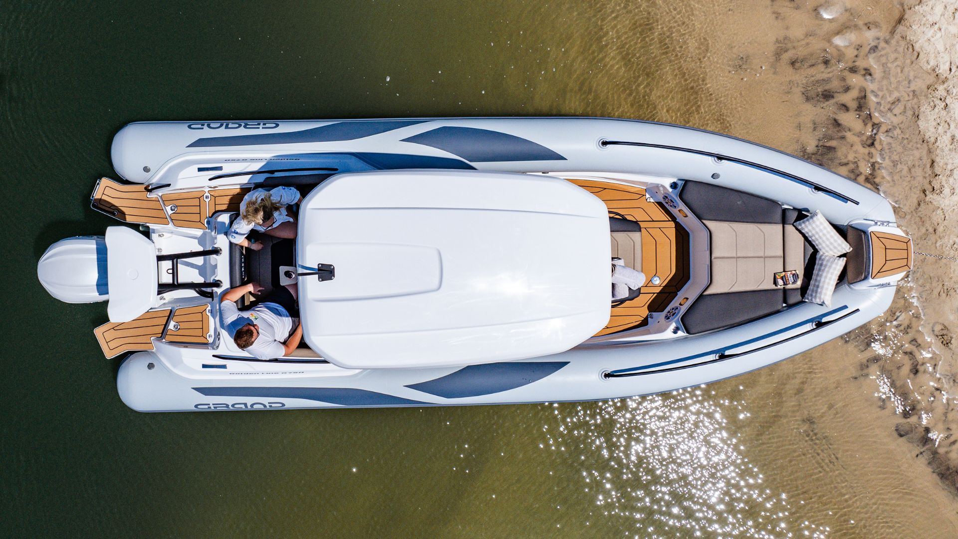 Grand G750 RIB boat beached on the sand with two passengers sat on the seating