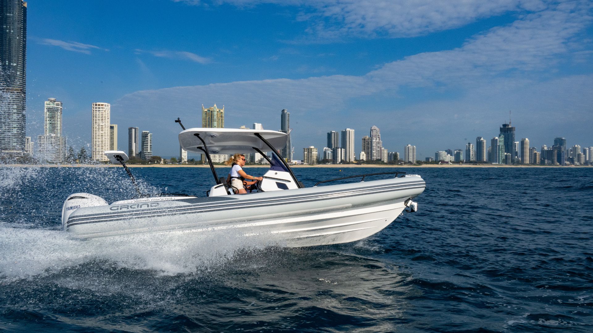 Grand G750 RIB boat on the water with a cityscape in the background, two passengers on board