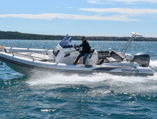 Centre console boat with white inflatable tubes and a passenger driving at an angle on the water.