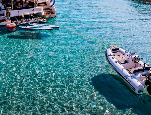 A Grand G380 - a yacht tender in the Grand RIBs range - with white tubes on light blue water, serving as a tender behind a catamaran yacht