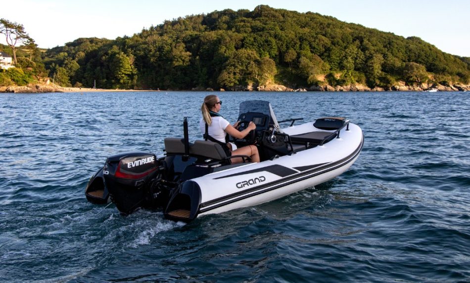 A white and black boat tender on the water with a female passenger at the helm